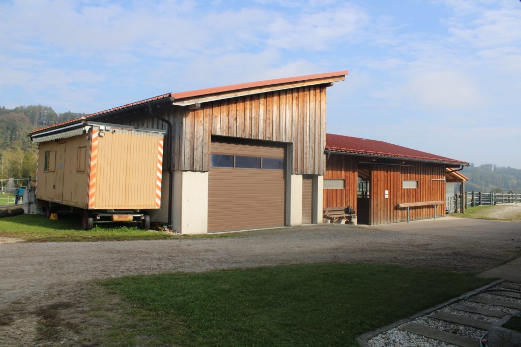 Sicht vom Parkplatz auf Maschinenhalle und Stallgebäude