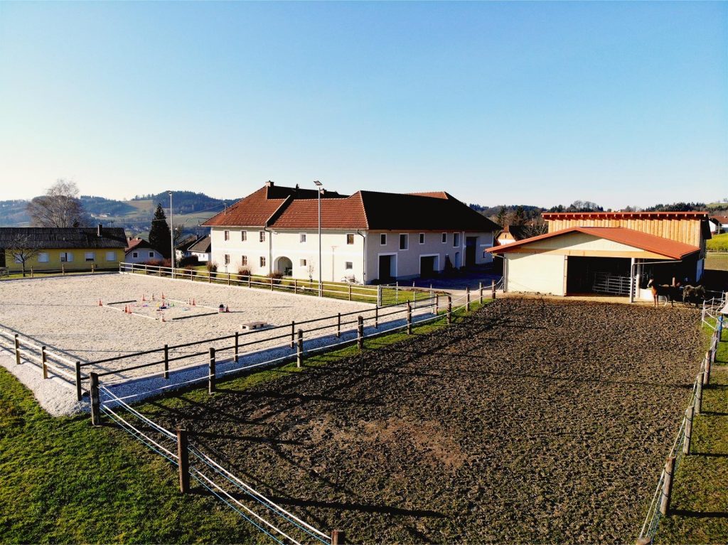 Drohnenbild von Charlie's Ranch mit Sicht auf Wohngebäude, Reitplatz, Stall und Koppel