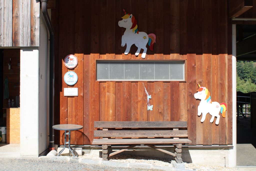 Holzbank vor Stall mit Reitabzeichen an der Wand und Einhornbildern