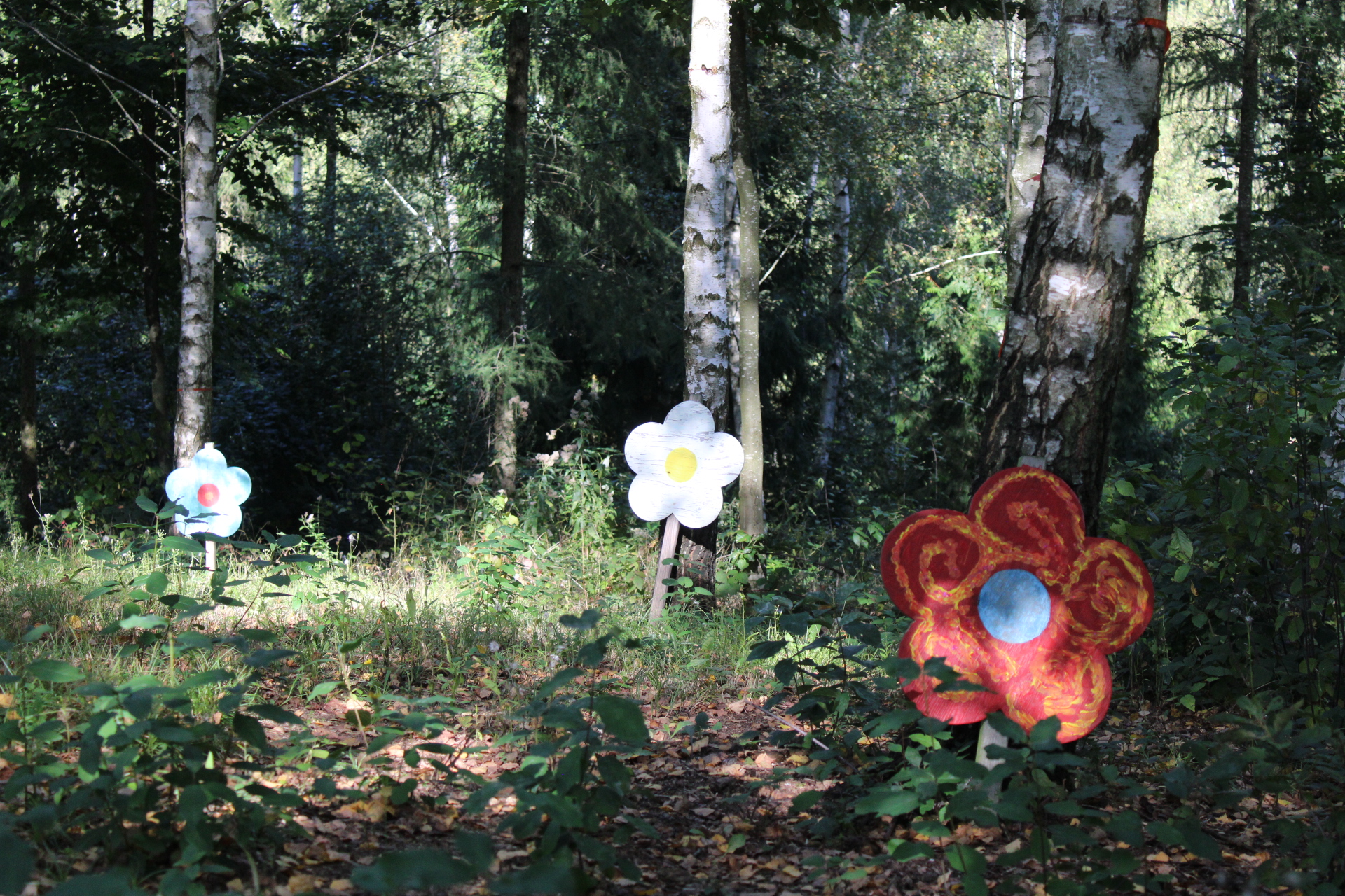 Waldabschnitt mit aufgestellten, bemalten Holzblumen